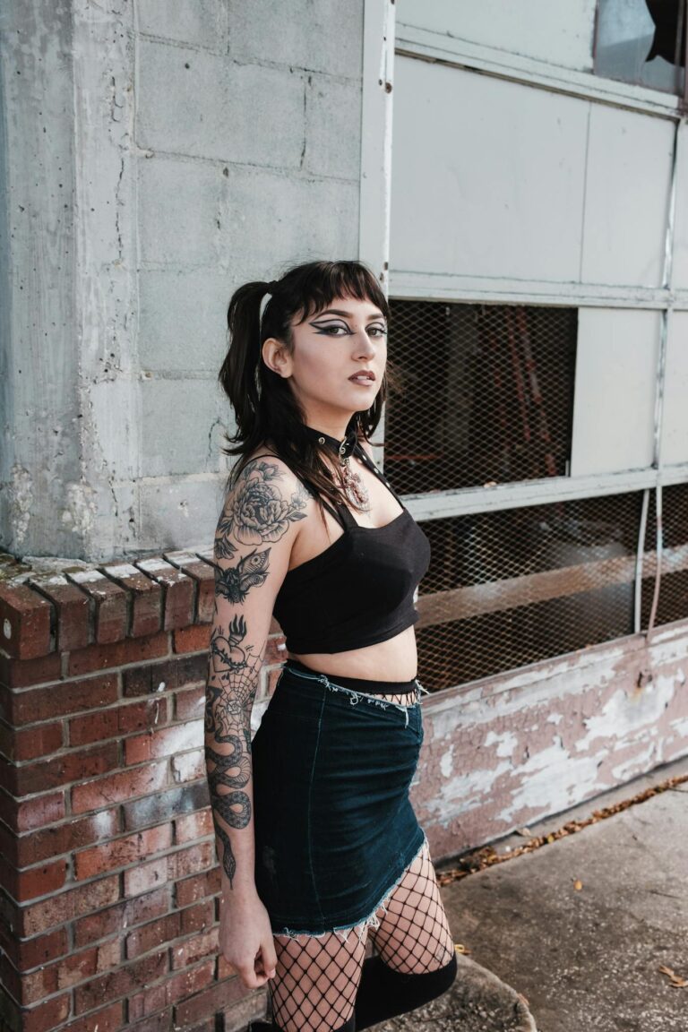 Stylish woman in urban setting wearing a crop top, skirt, and fishnet tights showing goth-inspired fashion.