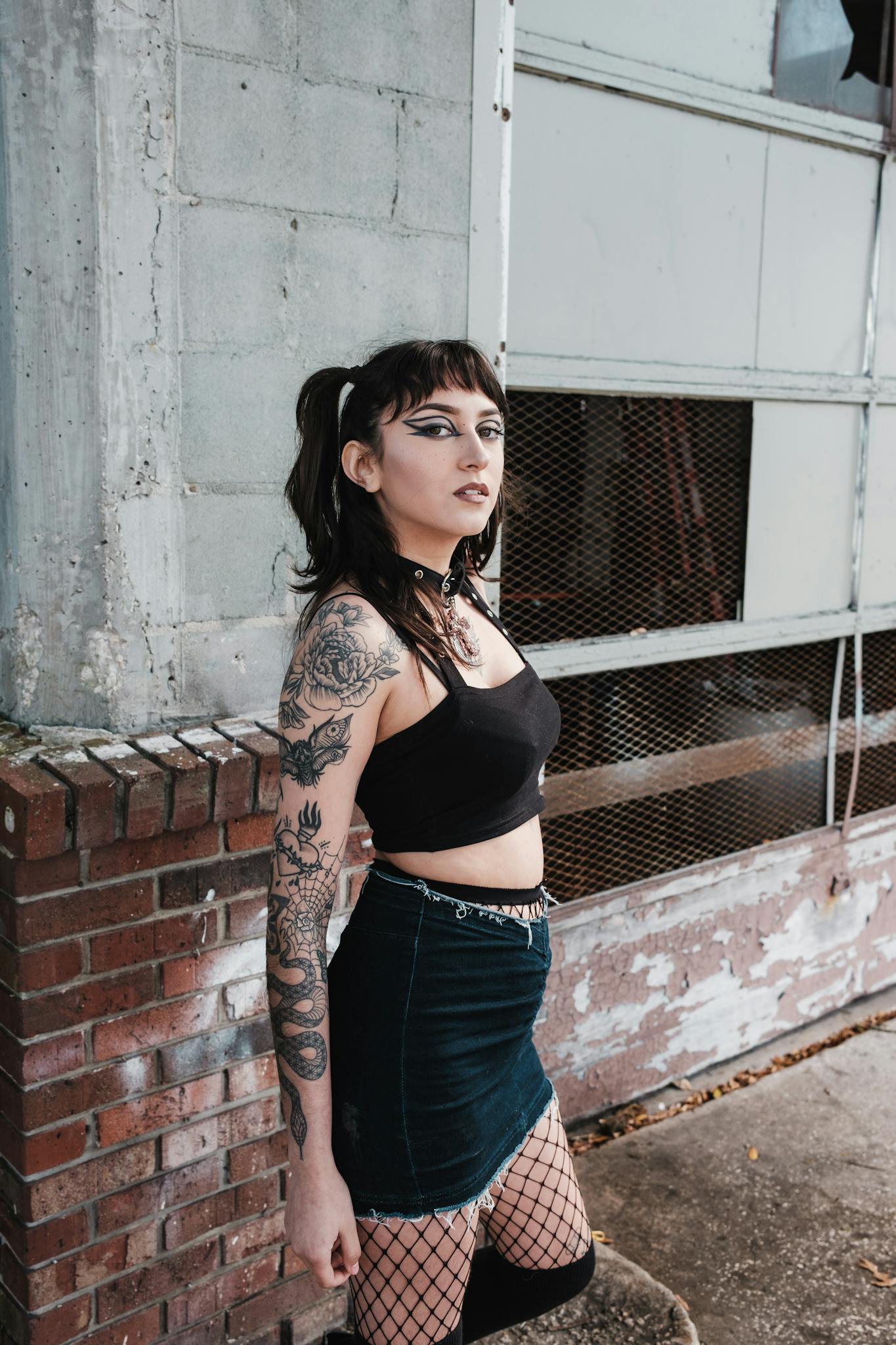 Stylish woman in urban setting wearing a crop top, skirt, and fishnet tights showing goth-inspired fashion.